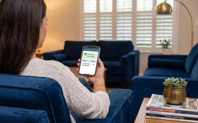 A homeowner paying their monthly HOA assessment online from the sofa, the portal showing a payment received confirmation